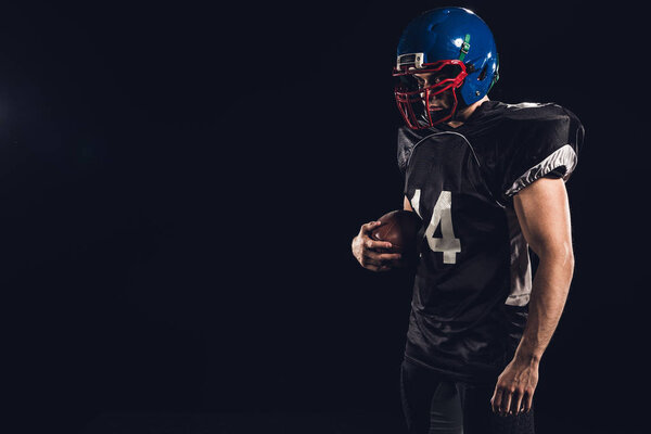 american football player in black uniform with ball in hand isolated on black