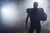 silhouette of american football player in uniform against white smoke