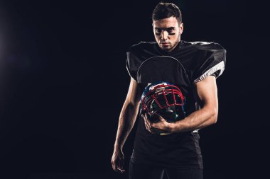 kask tutarak ve siyahta izole kamera seyir siyah üniformalı ciddi Amerikan futbolu oyuncusu