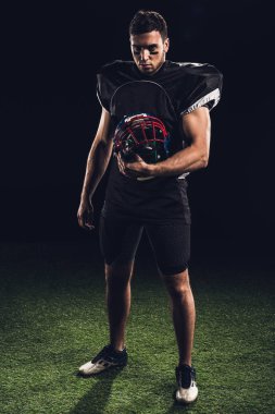 kask tutarak ve kameraya siyah üzerinde seyir siyah üniformalı ciddi Amerikan futbolu oyuncusu