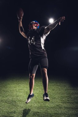 sahne ışıkları altında topu ile siyah üzerine atlama atletik Amerikan futbolu oyuncusu