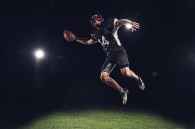 sahne ışıkları altında topu ile siyah üzerine atlama Amerikan futbolu oyuncusu