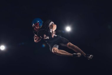 bottom view of american football player jumping with ball under spotlights on black clipart