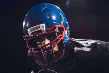 close-up portrait of serious american football player in helmet looking at camera isolated on black clipart