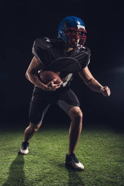 american football player holding ball and running on field on black clipart