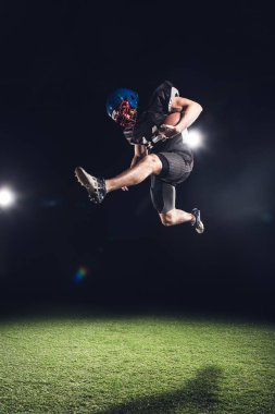 american football player jumping with ball over green grass on black