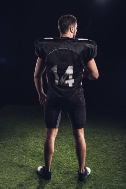 Amerikan futbolu oyuncusu çimenlerin üzerinde siyah üniforma ayakta siyah dikiz