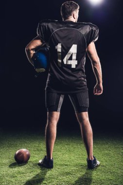 rear view of american football player with helmet standing on green grass on black clipart