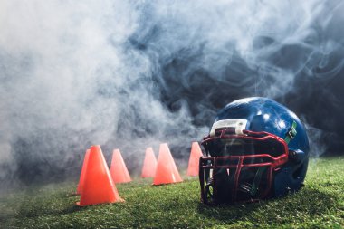 close-up shot of american football helmet with cones on green grass with white smoke above clipart