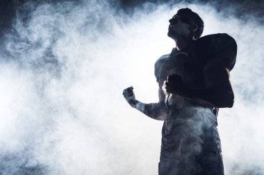 bottom view of emotional american football player making fists and looking up against white smoke
