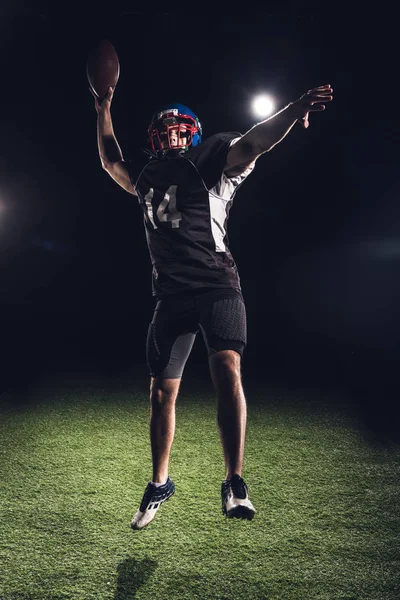 Athletischer American Football Spieler Springt Mit Ball Unter Scheinwerfern Auf — kostenloses Stockfoto