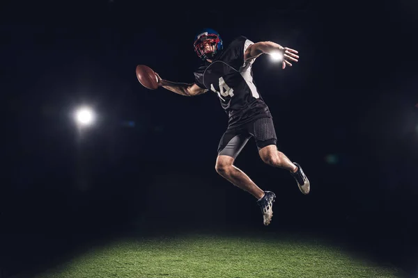 Jogador Futebol Americano Pulando Com Bola Sob Holofotes Preto — Fotografia de Stock