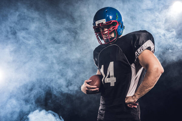 serious american football player with ball against white smoke