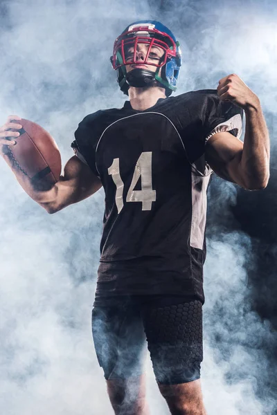 美国橄榄球运动员的底部看法与球葡萄干拳头反对白色烟雾 — 免费的图库照片