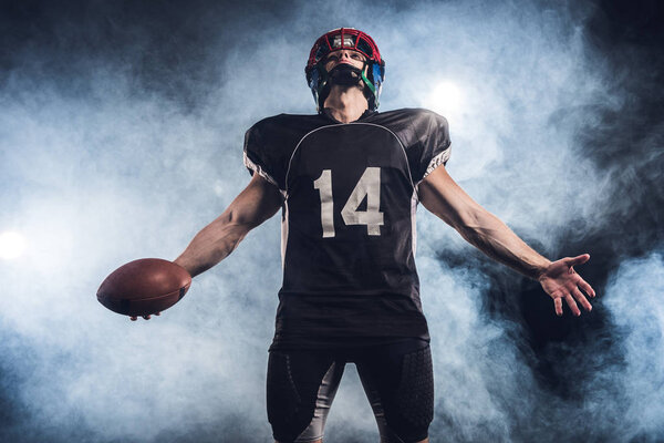 american football player with ball looking up against white smoke