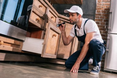 pest control worker examining kitchen with flashlight clipart
