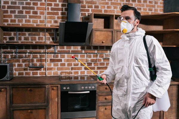 side view of pest control worker standing with sprayer in kitchen