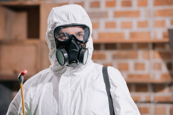 портрет работника по борьбе с вредителями, стоящего в респираторе и держащего распылитель на кухне
