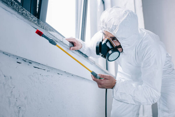 работник по борьбе с вредителями, распыляющий пестициды под подоконником дома
