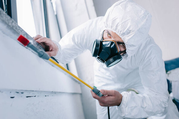 работник по борьбе с вредителями в респираторе распыления пестицидов под подоконником дома
