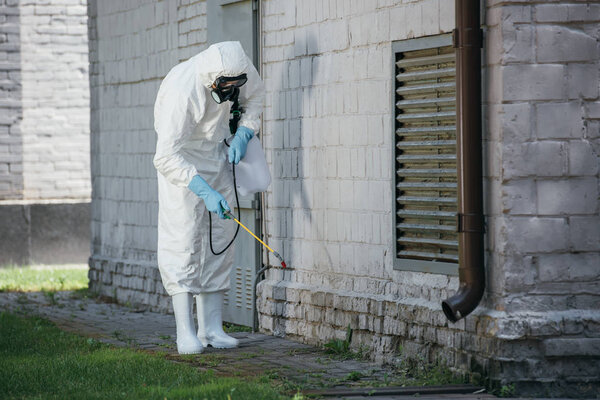 pest control worker spraying pesticides with sprayer on building wall