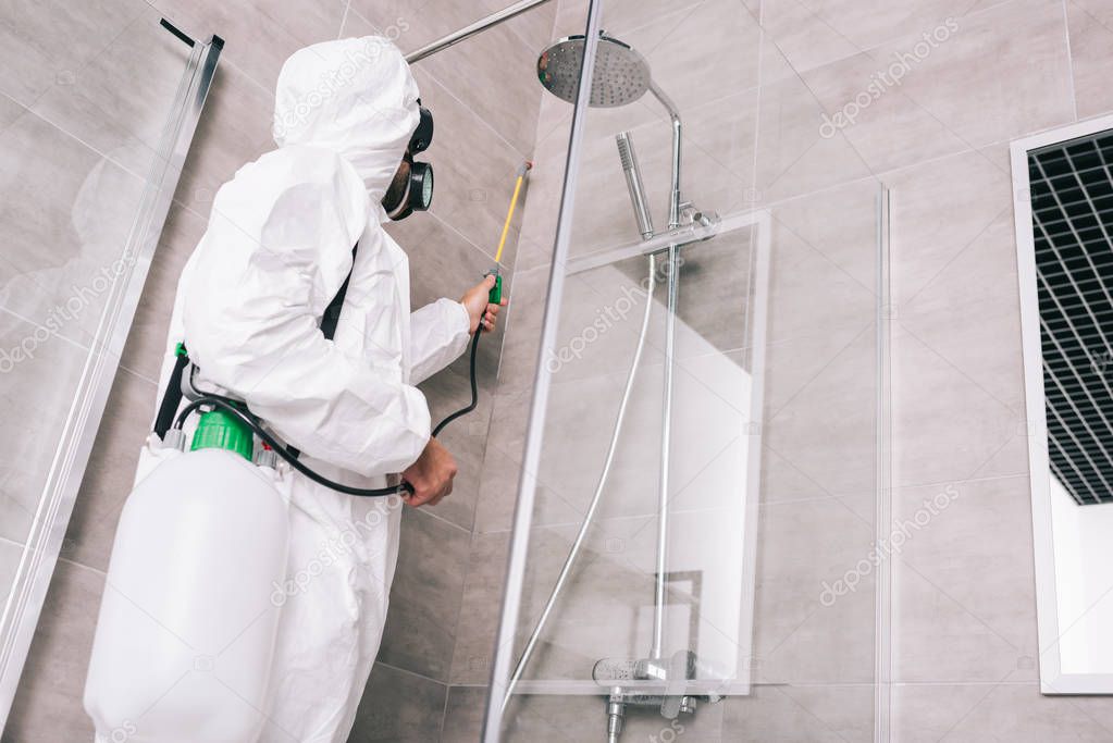 low angle view of pest control worker spraying pesticides with sprayer in bathroom