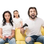 Happy man and upset family playing video games on yellow sofa isolated on white