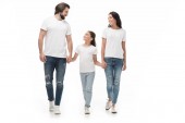 Lächelnde Familie in weißen Hemden und Jeans, Händchen haltend, während sie isoliert auf weißem Grund zusammen geht