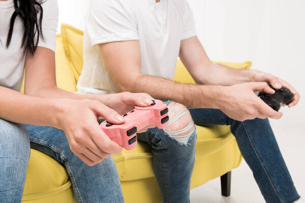 partial view of couple with gamepads sitting on sofa isolated on white