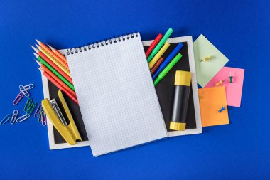 top view of blank notebook and empty blackboard with variety stationery on blue background 
