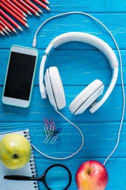 mavi ahşap arka plan üzerinde kulaklık, boş ekran, elma ve ileti örneği ile smartphone üstten görünüm 