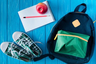 top view of sneakers, rucksack, empty notebook, apple and pencil on blue wooden background clipart