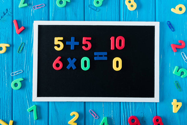 top view of blackboard with math sums, colorful numbers and paper clips on blue wooden background 