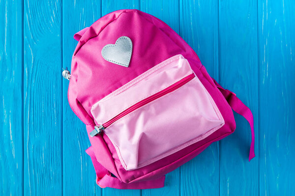 top view of pink backpack on blue wooden background