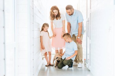 parents and children looking at adopted pug dog in corridor of animals shelter  clipart