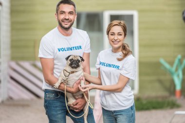 hayvan sığınak pug köpek ve kameraya bakarak tutan iki gönüllü 