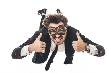 smiling young businessman in vintage aviation goggles falling and showing thumbs up isolated on white