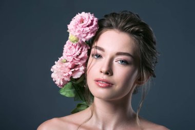 yakın çekim gri izole kamera bakarak kulağının arkasında pembe eustoma çiçeklerle çekici genç kadın portresi