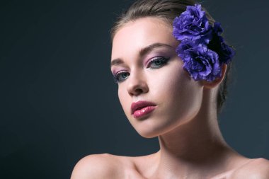 close-up portrait of seductive young woman with eustoma flowers behind ear looking at camera isolated on grey clipart