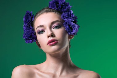 close-up portrait of attractive young woman with eustoma flowers on head looking at camera isolated on green clipart