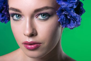 close-up portrait of beautiful young woman with eustoma flowers on head looking at camera isolated on green clipart
