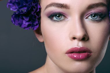 yakın çekim gri izole kamera bakarak kulağının arkasında eustoma çiçekli şehvetli genç kadın portresi