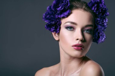 close-up portrait of beautiful young woman with eustoma flowers on head looking at camera isolated on grey clipart