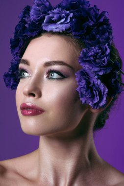 close-up portrait of beautiful young woman with eustoma flowers wreath on head looking away isolated on purple clipart