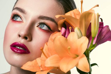 close-up portrait of beautiful young woman with stylish makeup and orange lilium flowers looking up isolated on white clipart