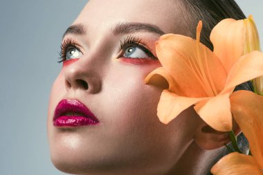 close-up portrait of beautiful young woman with stylish makeup and orange lilium flowers looking up isolated on grey clipart
