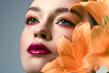 close-up portrait of beautiful young woman with stylish makeup and orange lilium flowers isolated on grey clipart