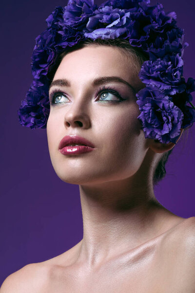 Крупным планом портрет привлекательной молодой женщины с венком из цветов эустомы на голове, смотрящей вдаль изолированной на фиолетовый
