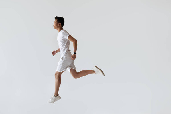 side view of young asian jogger running on grey background 