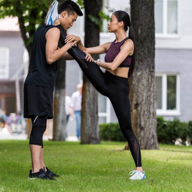 young asian sportsman helping female athlete to stretch on grass in park  clipart